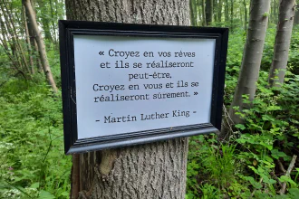 A sign on a tree cites Martin Luther King in French: “Croyez en vos rêves et ils se réaliseront peut-être. Croyez en vous et ils se réaliseron sûrement.”